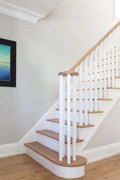 a white staircase with wooden handrails in a room next to a painting on the wall