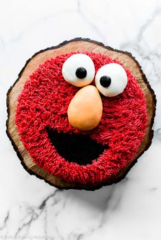 a red cake with eyes and nose on top of a white marble countertop next to a piece of wood