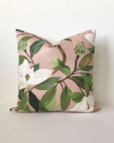 a pink pillow with white flowers and green leaves on it, against a white wall