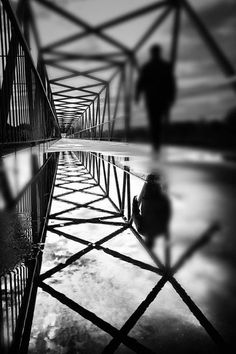 two people walking across a bridge with water reflecting them in the puddles on the ground