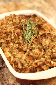 a casserole dish filled with stuffing and topped with a sprig of rosemary