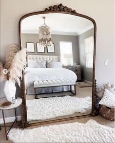 a large mirror sitting on top of a floor next to a white bed in a bedroom