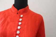 This is a great Vintage Women's Jan Barboglio Orange Linen Blouse Mother of Pearl Button Down Shirt from the 1980s.  The top is made of 100% linen and it has 12 mother of pearl buttons down the front.  This beautiful oriental style blouse is a size 10.  This shirt is in great shape with no holes or stains.  It measures 22 inches from pit to pit and 28 inches in length.  This gorgeous blouse would look great with any outfit! Summer Blouse With Stand Collar And Buttons, Stand Collar Blouse With Buttons For Summer, Classic Stand Collar Tops With Buttons, Vintage Summer Tops With Button Cuffs, Jan Barboglio, Gorgeous Blouses, Patterned Cardigans, Linen Blouse, Cute Sweaters