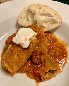 a white plate topped with cabbage covered in gravy next to a piece of bread