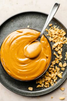 peanut butter in a bowl with peanuts scattered around it on a black plate next to a spoon