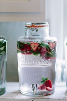 a jar filled with sliced strawberries sitting on top of a table next to two glasses