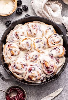 a pan filled with cranberry cinnamon rolls next to some berries and cream cheese