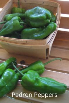 some green peppers are in a basket on a wooden table next to a bowl of them