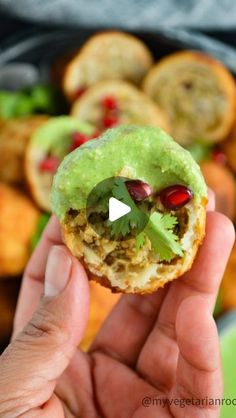 a person is holding up a small pastry with green toppings and pomegranates