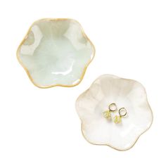 two small white dishes with gold trims on each one and an earring in the middle