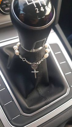 the interior of a car with a steering wheel knob and rosary bracelet on it's center console