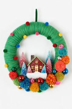 a christmas wreath hanging on the wall with ornaments around it and a house in the background