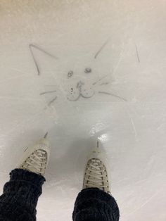 someone is standing on an ice rink with their feet in the snow and there is a cat drawn on the ice