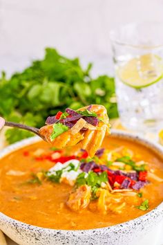 a hand holding a spoon full of soup and garnished with cilantro