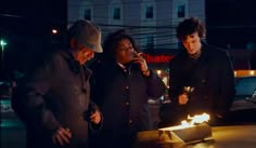 three people standing around a cake with lit candles