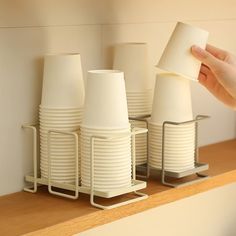 a hand is holding a paper cup over some cups on a shelf in a kitchen