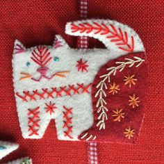 a cat ornament is hanging on a red cloth with white and orange designs