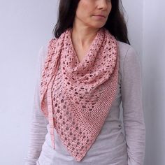 a woman wearing a pink crocheted shawl standing next to a white wall