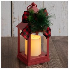 a red lantern with a pine tree in it on a wooden table next to a candle