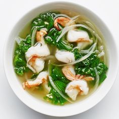 a white bowl filled with soup and shrimp on top of green vegetables in broth