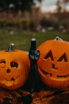 two carved pumpkins sitting on top of a wooden table next to a black bottle