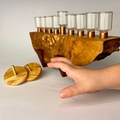 a hand is reaching for an object made out of wood and glass cups on it