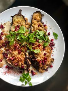 a white plate topped with eggplant covered in sauce and garnished with pomegranate