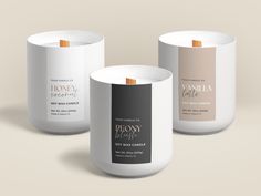 three candles with labels on them sitting side by side in front of a beige background