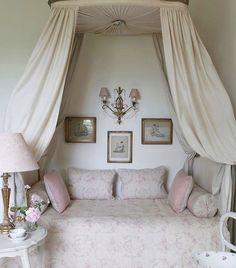 a white bed sitting under a canopy in a bedroom next to two pictures on the wall