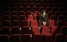 a woman sitting in the middle of an empty auditorium with rows of red chairs behind her