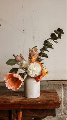 an arrangement of flowers in a white vase on a wooden table next to a brick wall