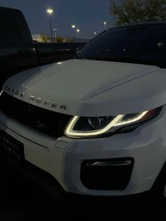 the front end of a white range rover parked in a parking lot at night with its lights on