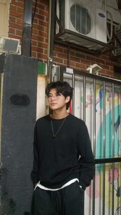 a young man standing in front of a brick wall with graffiti on the walls behind him