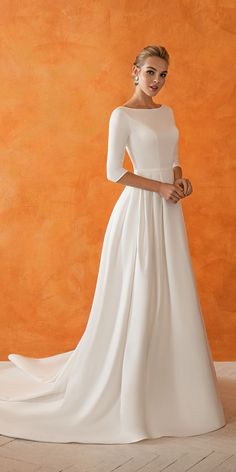 a woman in a white wedding dress standing against an orange wall