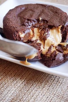 a white plate topped with a chocolate cookie covered in ice cream next to a spoon