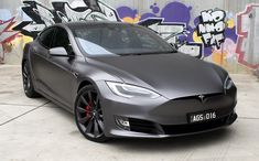 a grey tesla parked in front of a graffiti covered wall