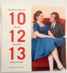 a wedding save the date card with a couple sitting on a red chair and holding each other's hand