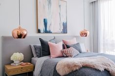 a bedroom with pink and grey decor on the walls, gray bedding, white pillows, and gold accents