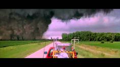 a large black cloud is in the sky above a red truck and green grass field