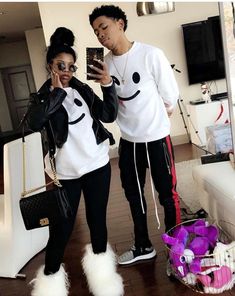 two people standing in a living room looking at a cell phone and wearing matching outfits