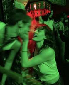 a group of people standing around in a room with red lights on the wall and one woman holding her hand up to her mouth