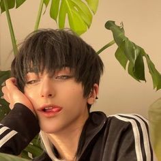 a person sitting at a table with a plant in the background and one hand on his head