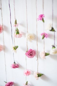 pink and white flowers hanging from strings on a wall with string attached to it's sides