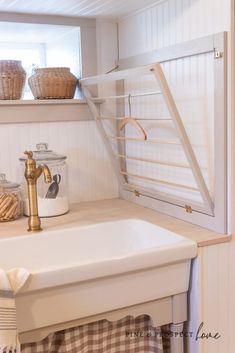 a white sink sitting under a window next to a shelf filled with baskets and other items