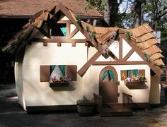 a house made out of cardboard with windows and plants on the roof, sitting in front of a tree