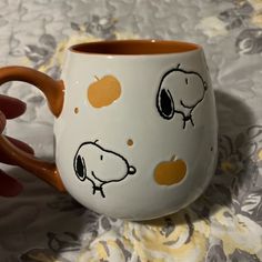 a hand holding a coffee cup with peanuts on it and orange rims, sitting on a tablecloth