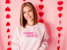 Get ready to level up your gaming style with our pink "Game Over" crewneck!  Made from a soft, high-quality material, this sweatshirt is comfortable to wear all day long.  But what sets these tops apart is the pink "Game Over" graphic on the front, while the glittering hearts add a touch of sparkle to your outfit.  GILDAN CREWNECK  Relaxed fit. Unisex sizing. Medium weight. Fleece lining.  50% cotton, 50% polyester WASHING INSTRUCTIONS -Turn clothes inside out -Machine wash cold only -Do not iro Valentine's Day Pink Sweatshirt With Letter Print, Valentine's Day Pink Letter Print Sweatshirt, Pink Crew Neck Sweatshirt For Valentine's Day, Valentine's Day Pink Crew Neck Sweatshirt, Casual Pink Sweatshirt For Valentine's Day, Casual Pink Valentine's Day Sweatshirt, Cute Pink Sweatshirt For Valentine's Day, Pink Kawaii Crew Neck Sweatshirt, Playful Pink Sweatshirt With Letter Print