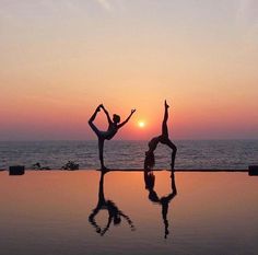 two people doing yoga on the edge of a swimming pool at sunset, with their arms in the air