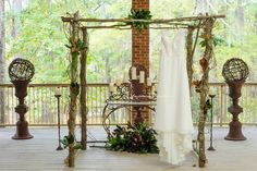 a wedding dress hanging from a wooden arbor on a porch in front of an outdoor fireplace