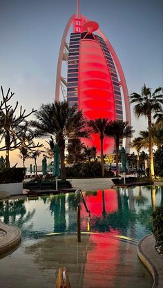 the burj building is lit up in red and blue at dusk, with palm trees surrounding it